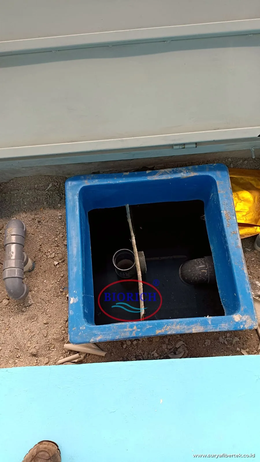 Grease trap fiberglass kecil bersekat yang ditanam di tanah, dengan pipa masuk dan keluar